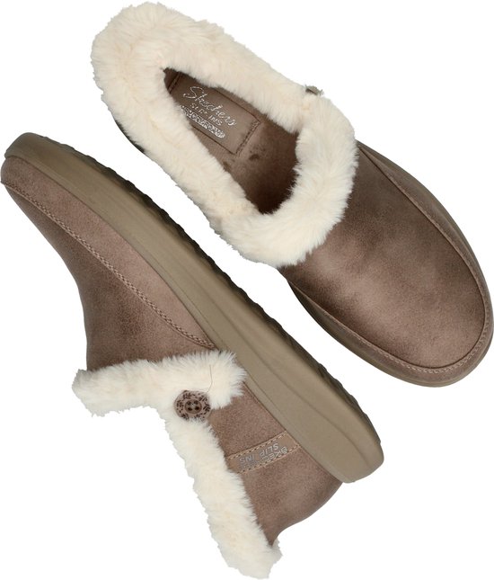 Taupe pantoffels met witte, fluffy voering en een decoratieve knoop aan de zijkant.