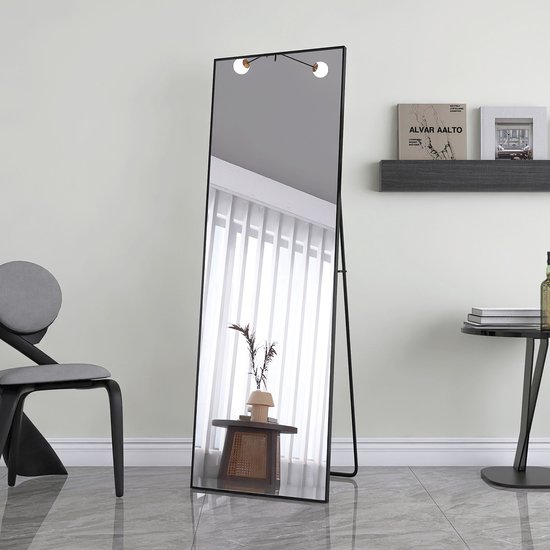 Een staande spiegel met zwart frame en ingebouwde lampjes, in een minimalistische kamer.