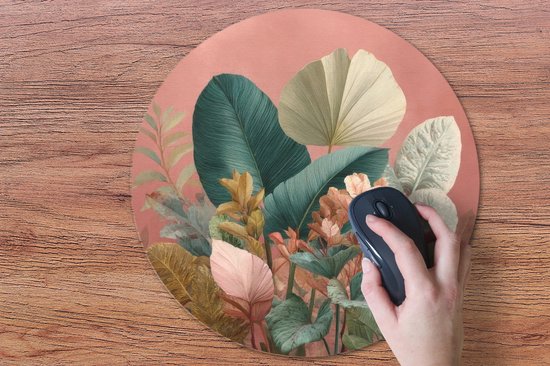 Ronde muismat met tropische bladeren print, roze achtergrond, met een hand die een muis bedient.