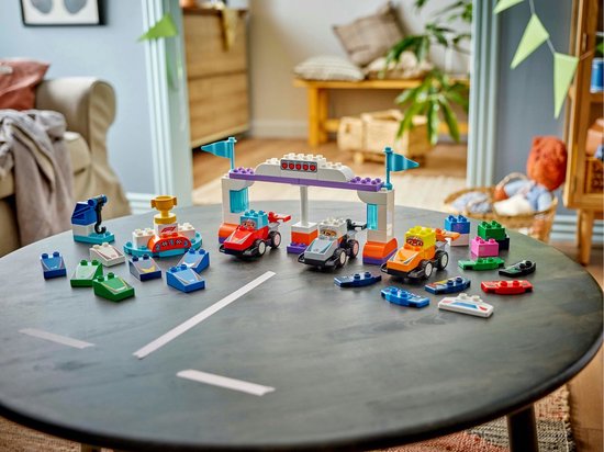 Piste de course LEGO Duplo avec des voitures, des drapeaux et des accessoires sur une table.