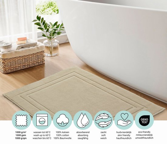 Beige badmat van 100% katoen in een badkamer met een witte badkuip. Iconen tonen 1000 g/m², wasbaar tot 60°C, 100% katoen, absorberend, zacht, huidvriendelijk en Oeko-Tex.