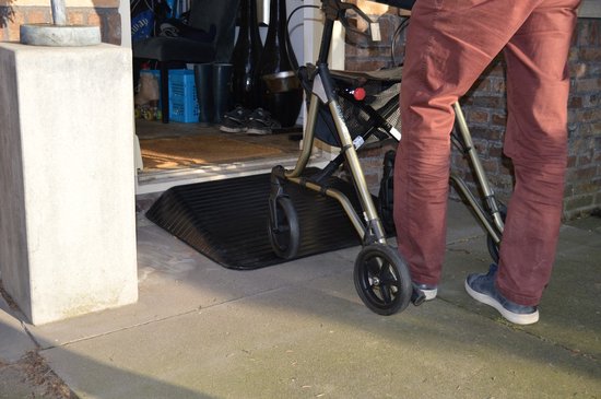 Zwarte rubberen drempelhulp met ribbelprofiel, voor een drempel van 25 mm hoog. Een persoon met een rollator staat op de drempelhulp.