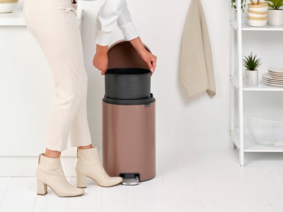 Vrouw doet bruine afvalzak in bruine prullenbak met open deksel. Ze staat in een keuken.