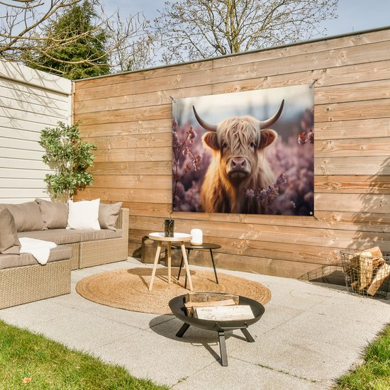 Tuinposter met Schotse hooglander in bloemen op een houten schutting naast een lounge set.