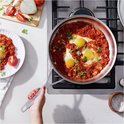 Hand wordt gebruikt om roestvrijstalen koekenpan met shakshuka en koriander vast te houden.