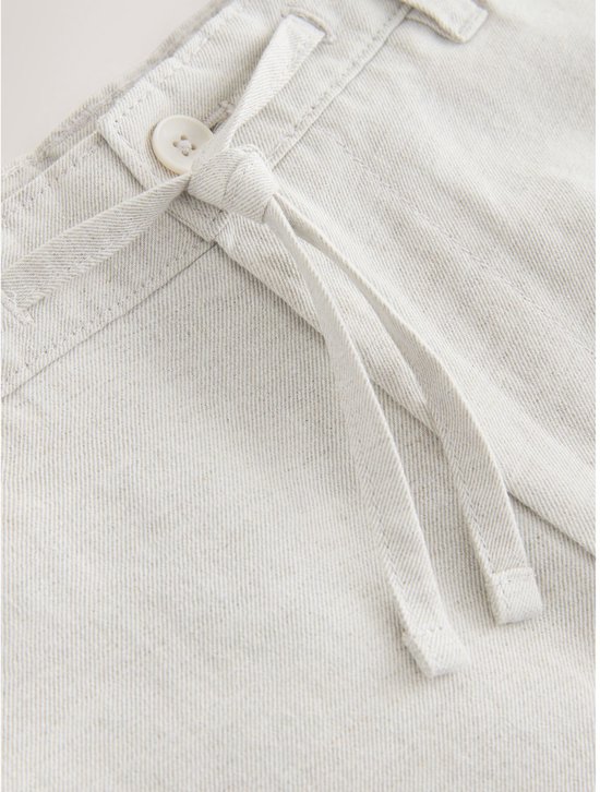 Detail van de tailleband van een lichtgrijze chino met katoen en linnen, met ceintuur en knoop.