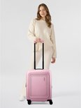 Vrouw met een crème outfit, met een roze American Tourister koffer.