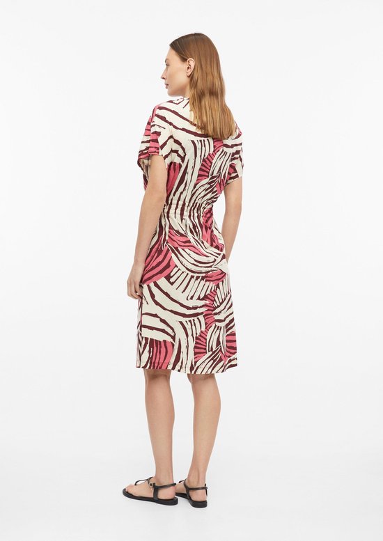 Model draagt een off-white T-shirtjurk met bruine en roze abstracte print, wijde mouwen en ceintuur in de taille.