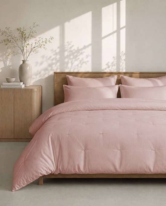 Roze dekbed met kussens op een houten bed. Het dekbed heeft stiksels.
