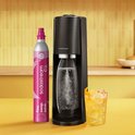 Zwarte Sodastream met roze CO2-cilinder en glas met bruiswater en ijs.
