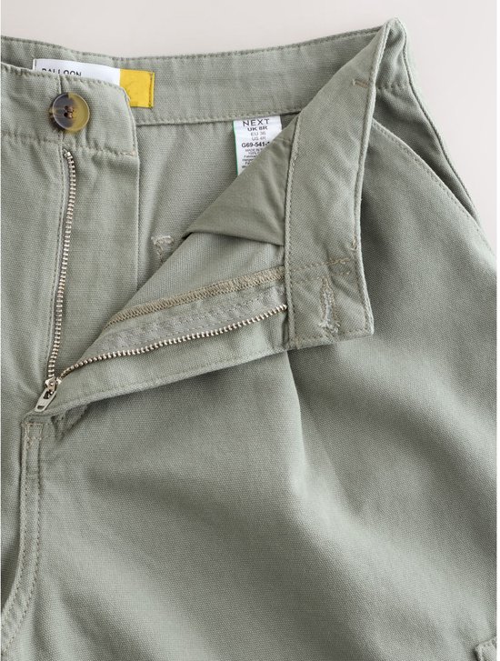 Gedetailleerde close-up van de gulp van een olijfgroene cargo broek, met knoop en rits.