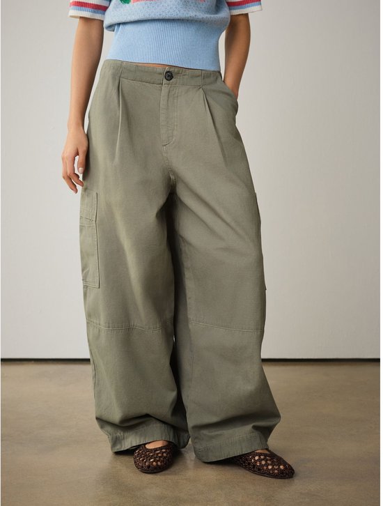 Model van voren in een olijfgroene wijde cargo broek met plooien en opgestikte zakken.