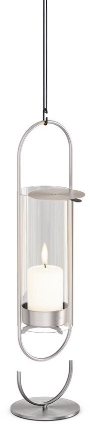 Een glazen windlicht met gouden frame hangt aan een koord, met een losse voet ernaast. Een witte kaars brandt.