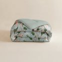 Een gevouwen lichtgroen dekbed met een print van roze en oranje bloemen en groene bladeren.