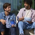 Deux hommes à l'extérieur, l'un tenant un pot à déjeuner et une cuillère bleus, l'autre une boîte à déjeuner bleu clair.