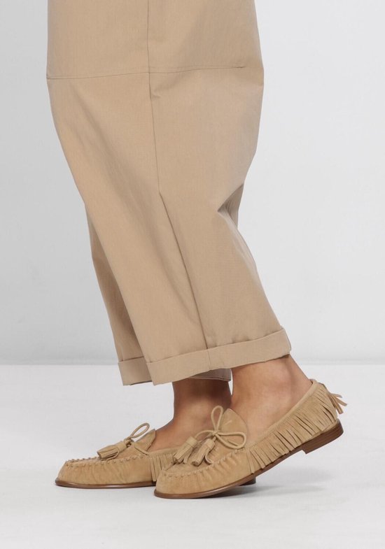 Voeten van een vrouw in beige instappers met franjes.