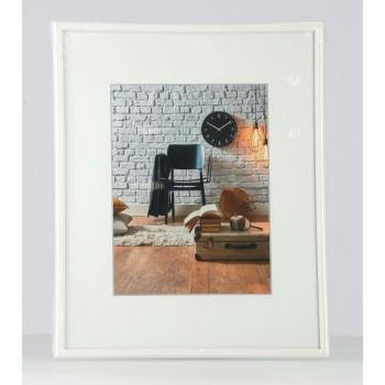 Witte fotolijst met een passe-partout, waarin een stilleven met stoel, klok en koffer.