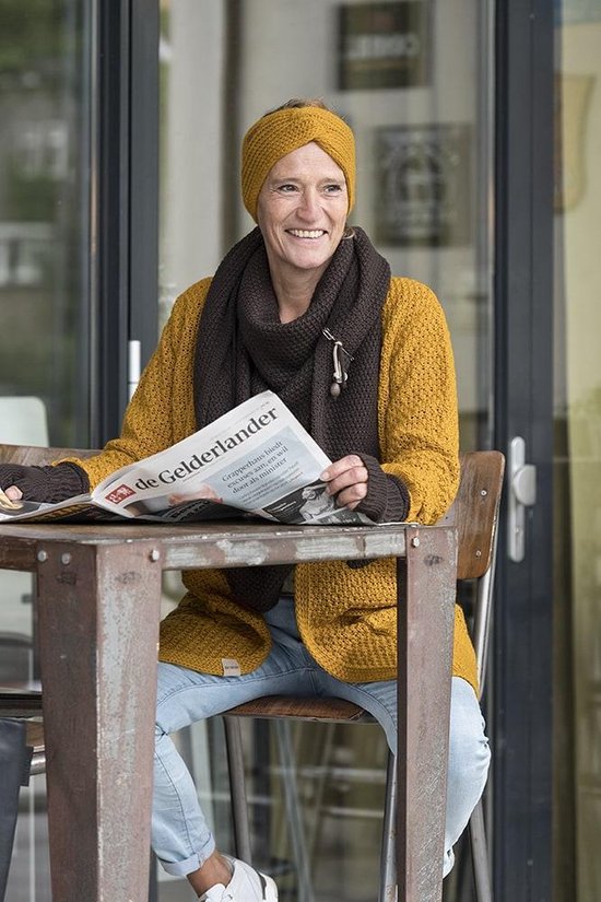 Model draagt een mosterdgeel gebreid vest met twee steekzakken en een donkerbruine sjaal.