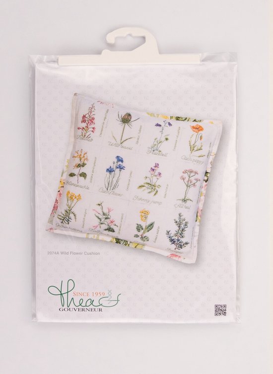 Un emballage contenant un coussin avec des broderies en point de croix de fleurs sauvages.