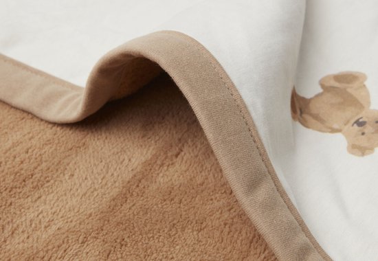 Détail du bord retourné d'une couverture pour bébé, montrant la doublure en polaire marron et la couche de coton blanche à imprimé ours en peluche.