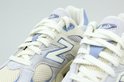 Close-up van de veters en de 'N'-logo's op twee lichtgrijze New Balance 9060 sneakers met lichtblauwe details.