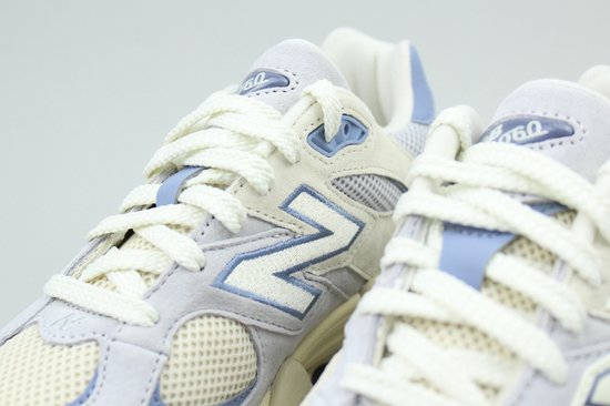 Close-up van de veters en de 'N'-logo's op twee lichtgrijze New Balance 9060 sneakers met lichtblauwe details.