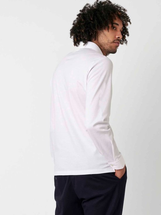 Man in wit longsleeve poloshirt en donkerblauwe broek, kijkend naar de zijkant.