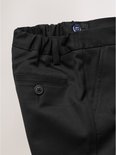 Detail van de voorkant van een zwarte broek met knoop en steekzak.