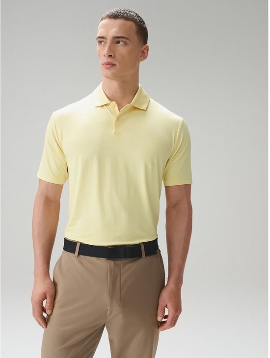 Man in een geel poloshirt met mesh-structuur, zwarte riem en beige broek.