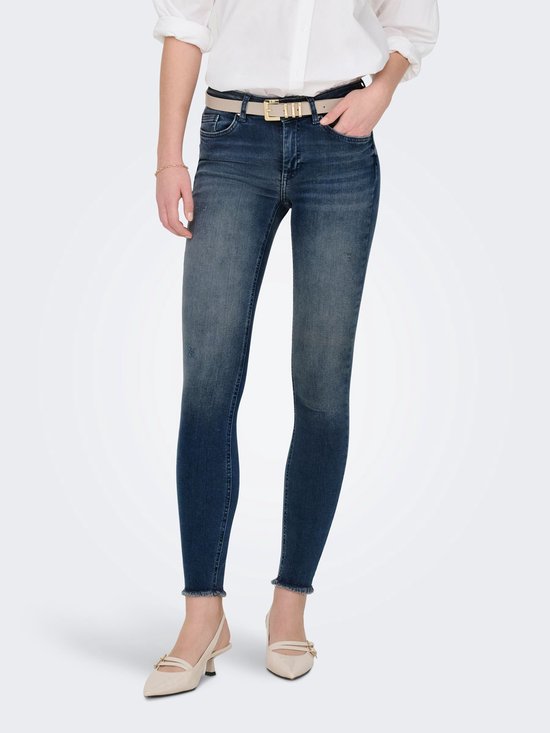 Model in een blauwe skinny jeans met rafels aan de zoom, gedragen met een beige riem.