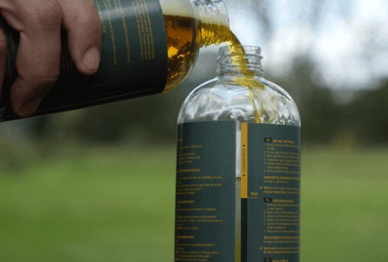 Hand giet U-Sport Bio Bike Cleaner Concentrate uit een fles in een andere fles. Groen en geel label met instructies.
