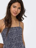 Close-up van een vrouw met lange bruine haren, draagt een marineblauwe jurk met spaghettibandjes en een witte geometrische print.