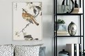 Une estampe japonaise d'un oiseau sur une branche fleurie, accrochée au-dessus d'un canapé à côté d'une étagère métallique.