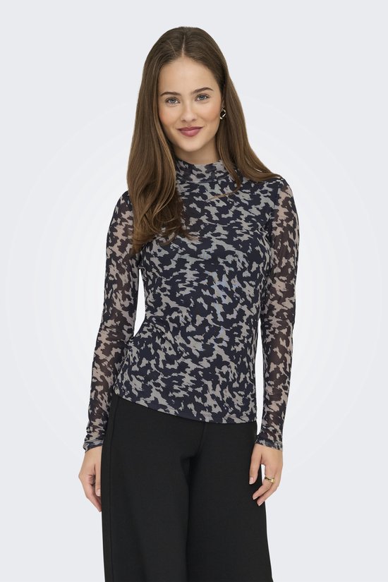 Model in longsleeve met hoge hals, abstracte print in nachtblauw en beige, met zwarte broek.