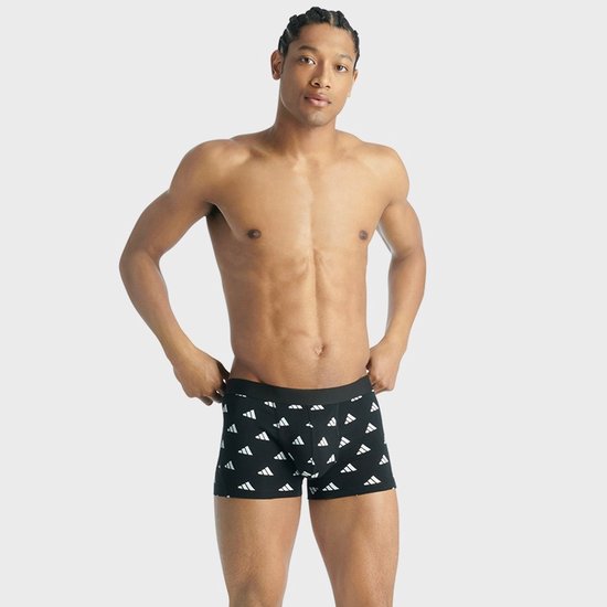 Man met zwarte boxershorts met een all-over print van witte Adidas-logo's.