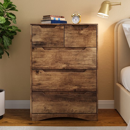 Commode marron clair à 5 tiroirs, avec un réveil et des livres. Texture grain de bois.