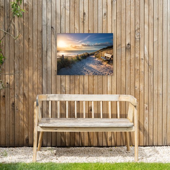 Canvasprint van een zonsondergang op het strand met duinen en een bankje, hangend aan een houten schutting met een houten bank ervoor.