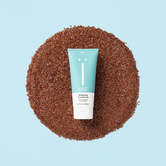Een turquoise tube Naïf conditioner, staand in een cirkel van lijnzaad, op een lichtblauwe achtergrond.