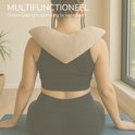 Zijaanzicht van vrouw met dreadlocks die een beige hartvormig verzwaringskussen om haar nek draagt, zittend op een yogamat.