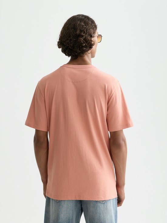 Model op de achterkant, draagt een perzikkleurig T-shirt met korte mouwen en jeans.