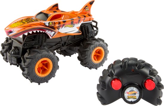 Oranje Hot Wheels Monster Truck met haaienthema en tijgerprint, met zwarte banden en oranje velgen, naast een zwarte afstandsbediening.