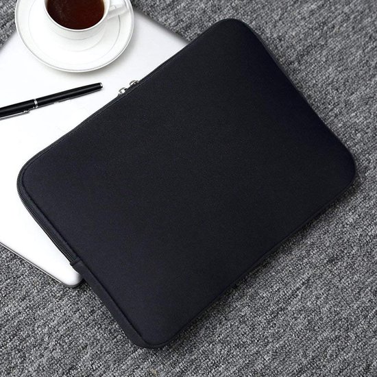 Housse d'ordinateur portable noire sur un tapis gris à côté d'un ordinateur portable, avec une tasse de café et un stylo