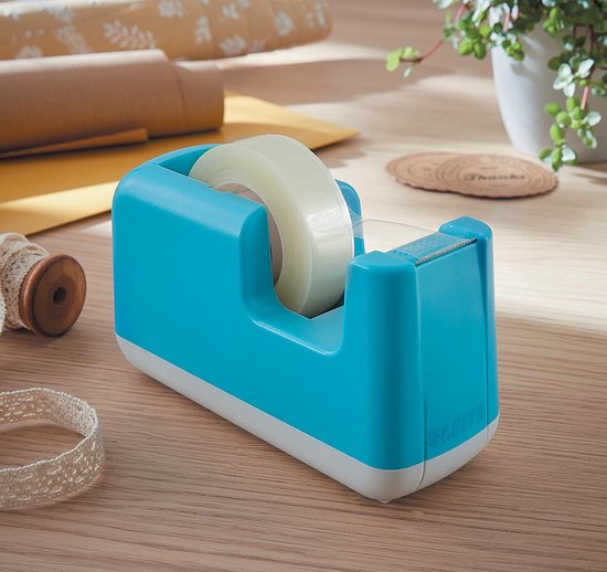 Turquoise Leitz plakbandhouder met witte basis op een houten bureau, omringd door cadeaupapier en lint.
