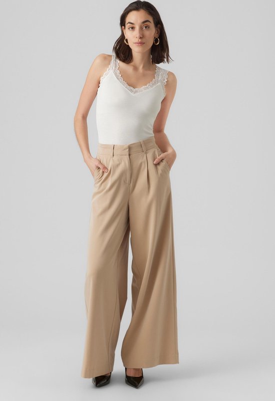 Model draagt een wit kanten hemdje met V-hals en beige wijde broek.