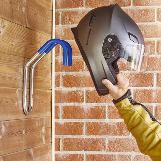 Hand met gele jas houdt grijze helm bij een zilverkleurige fietshaak.
