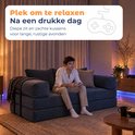 Man speelt videogames op een blauwe corduroy bank in een sfeervol verlichte kamer.