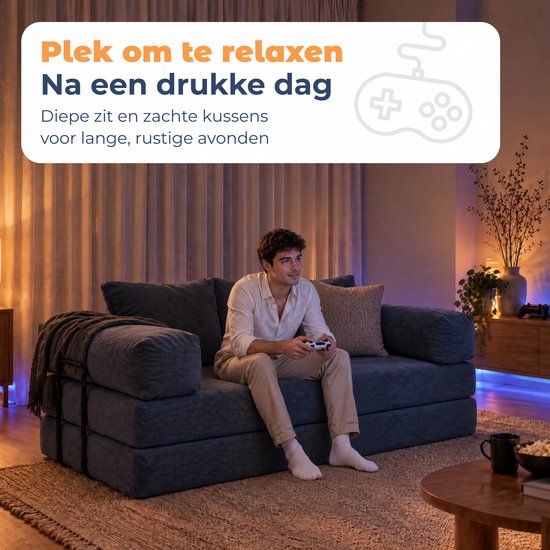 Man speelt videogames op een blauwe corduroy bank in een sfeervol verlichte kamer.