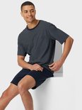Model zittend in een marineblauwe pyjama met fijn ruitpatroon en effen short.