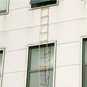 Een brandtrap met witte en blauwe touwen en houten sporten hangt langs een wit gebouw.