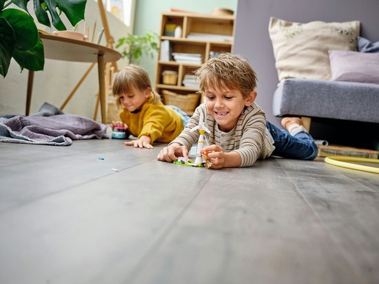 Twee kinderen spelen op de grond met een LEGO-windmolen en een blauw-witte auto.